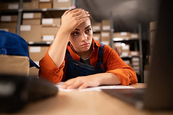 Warehouse worker on laptop while sitting at her working place. Tired woman working too long at computer.
